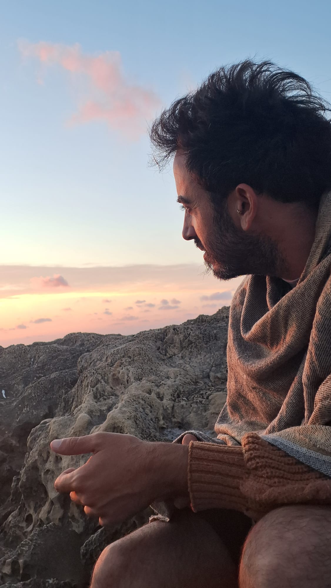 זוהר עמר יושב על סלעים מול הים באור שקיעה