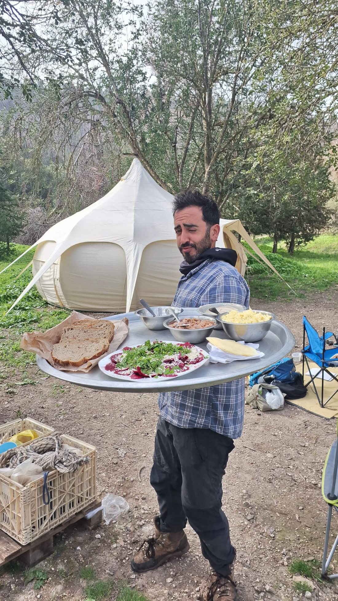 זוהר עמר נושא מגש גדול עם מנות בישול שטח, על רקע אוהל בחורש